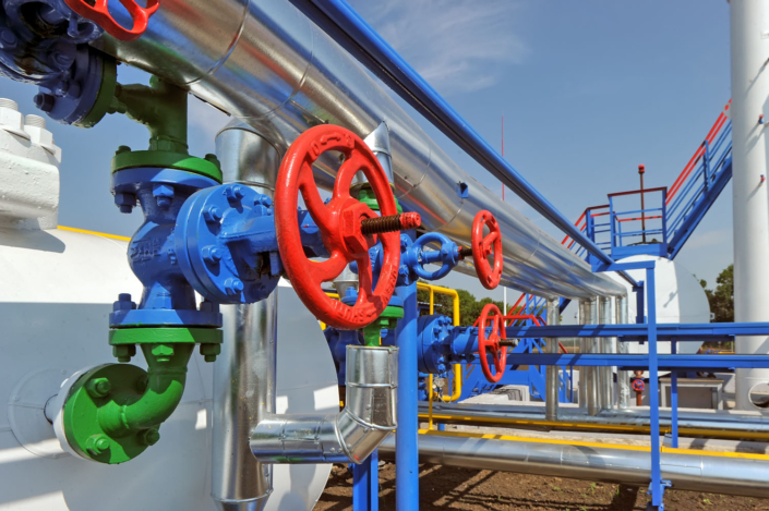 Red gate valve with steel pipe in natural gas compressor station in bright sunny summer day